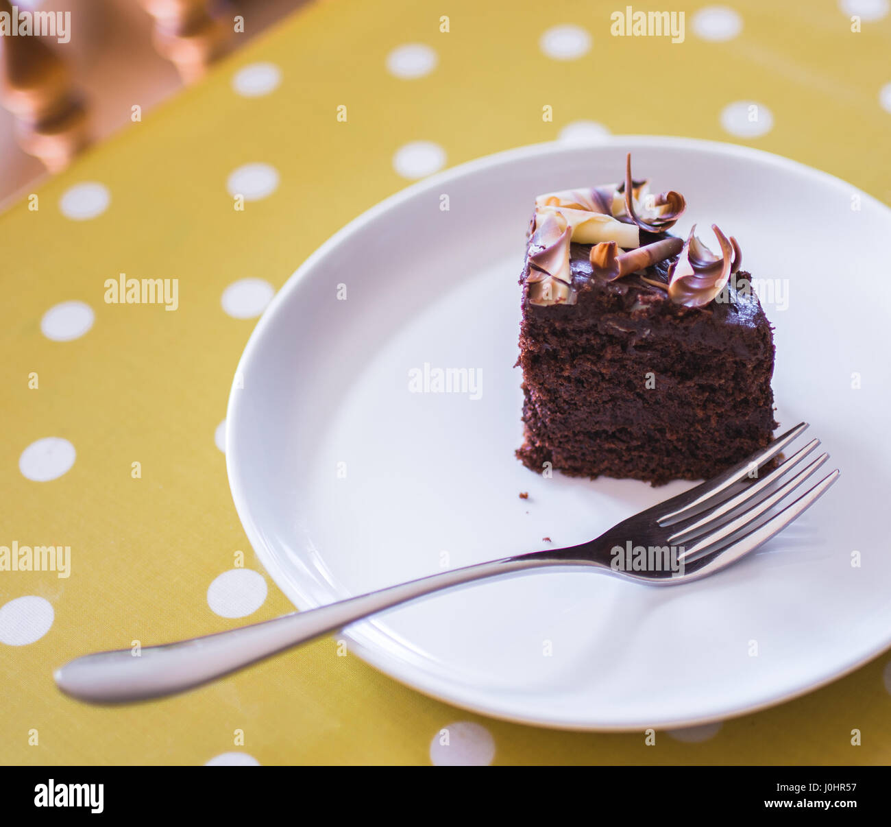 Torta al cioccolato fetta servita su una piastra bianca con giallo polka dot tovaglia Foto Stock
