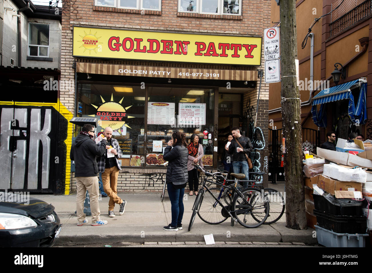 In Canada, a Toronto. Kensington market, quartiere multiculturale . I clienti a mangiare le polpette di fronte al Golden Patty panificio. Foto Stock