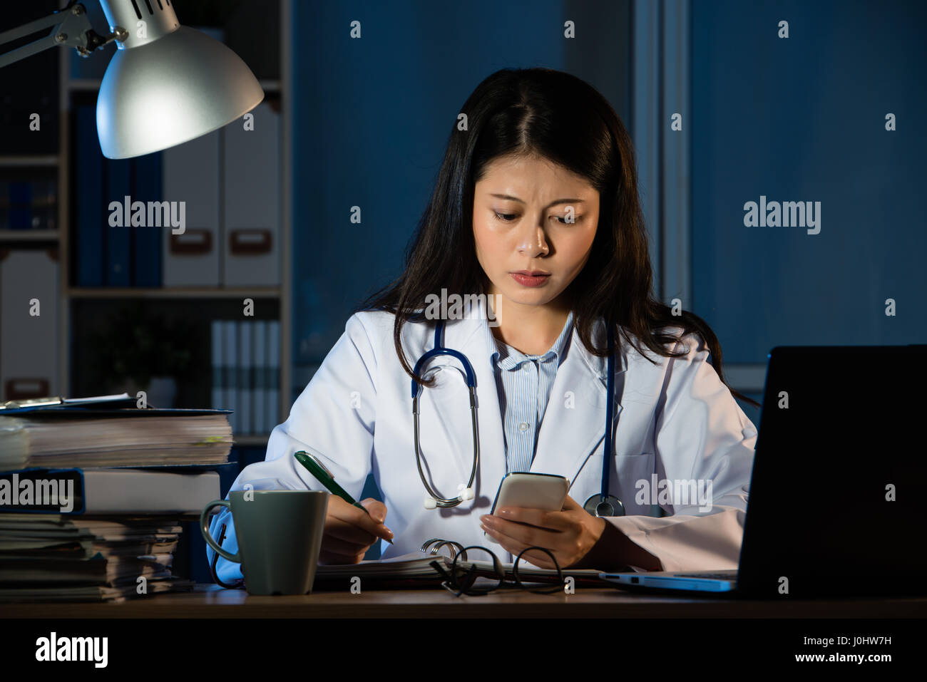 Stanco giovane medico donna ricevuto cattive notizie dal messaggio di smartphone a tarda notte. piuttosto razza mista asian donna cinese modello. medici e di salute con Foto Stock