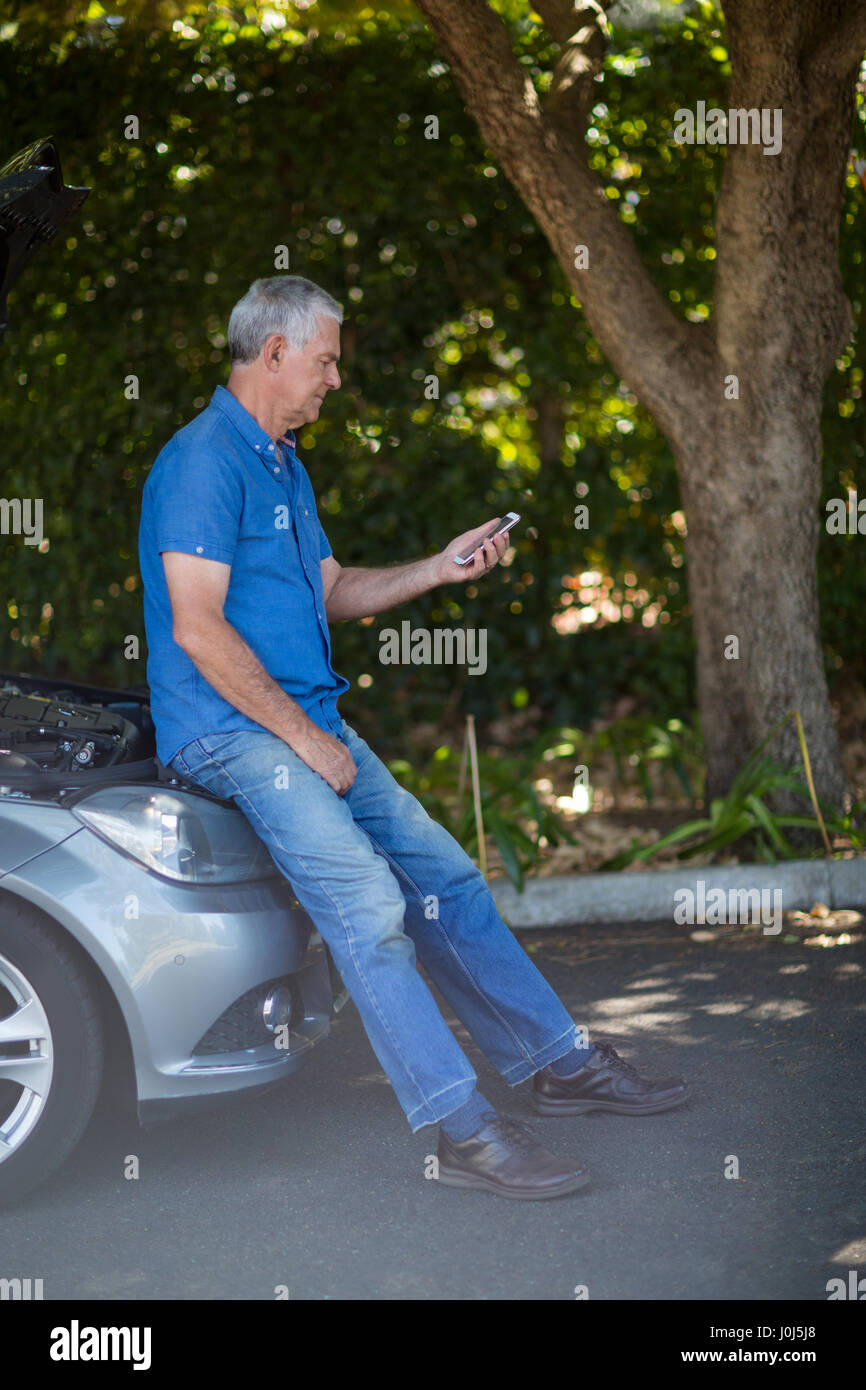Senior un uomo guarda il telefono cellulare dopo la ripartizione per auto Foto Stock