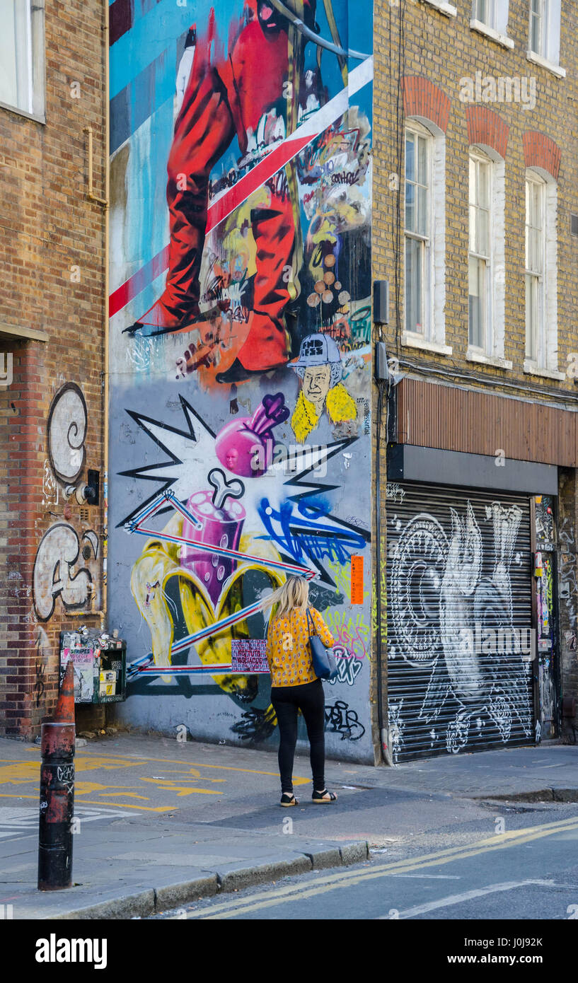 Una donna cammina davanti a una grande parete su Hanbury Street nella zona est di Londra che è coperto di arte di strada. Foto Stock