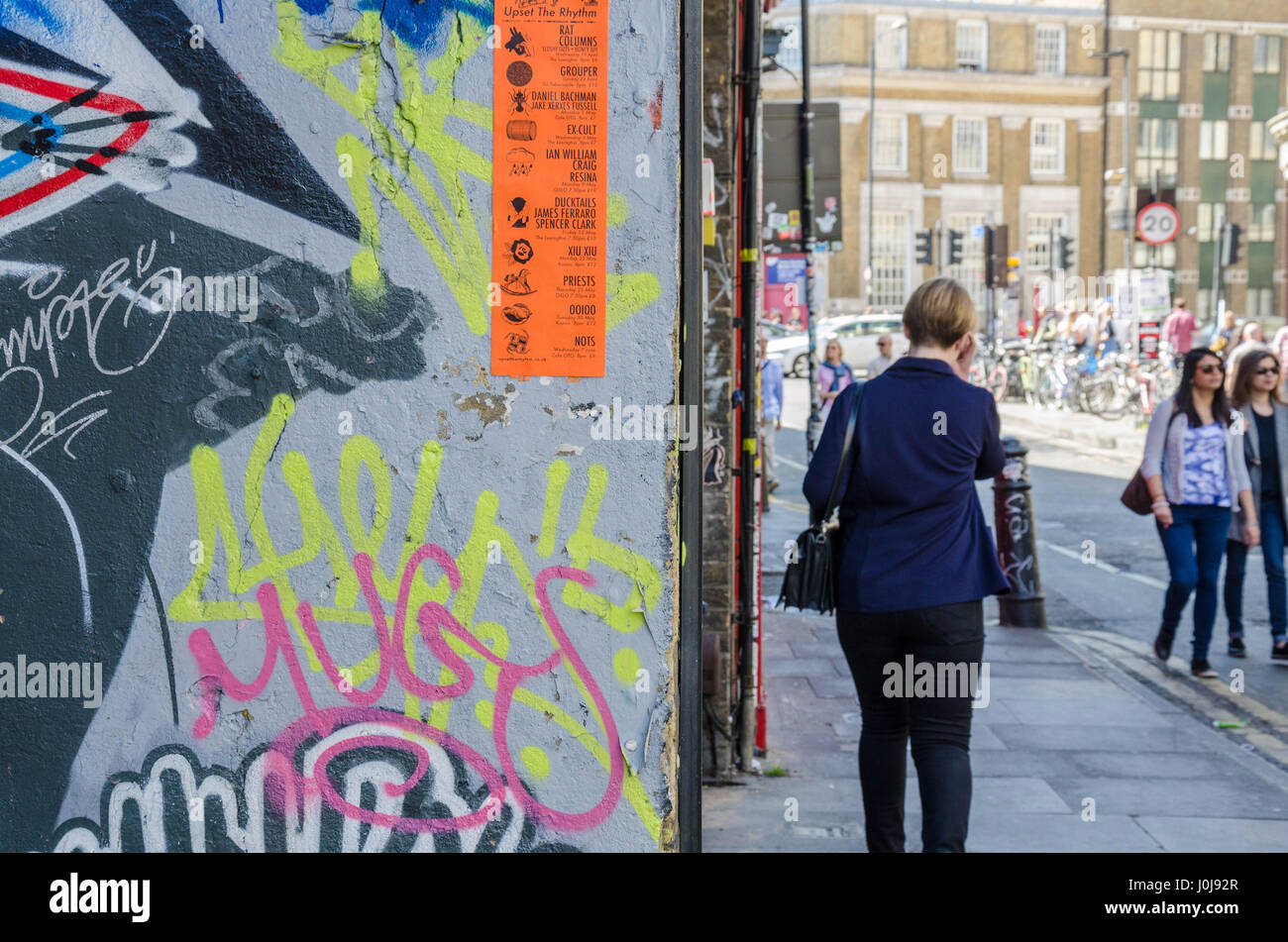 Una donna cammina davanti a una grande parete su Hanbury Street nella zona est di Londra che è coperto di arte di strada. Foto Stock