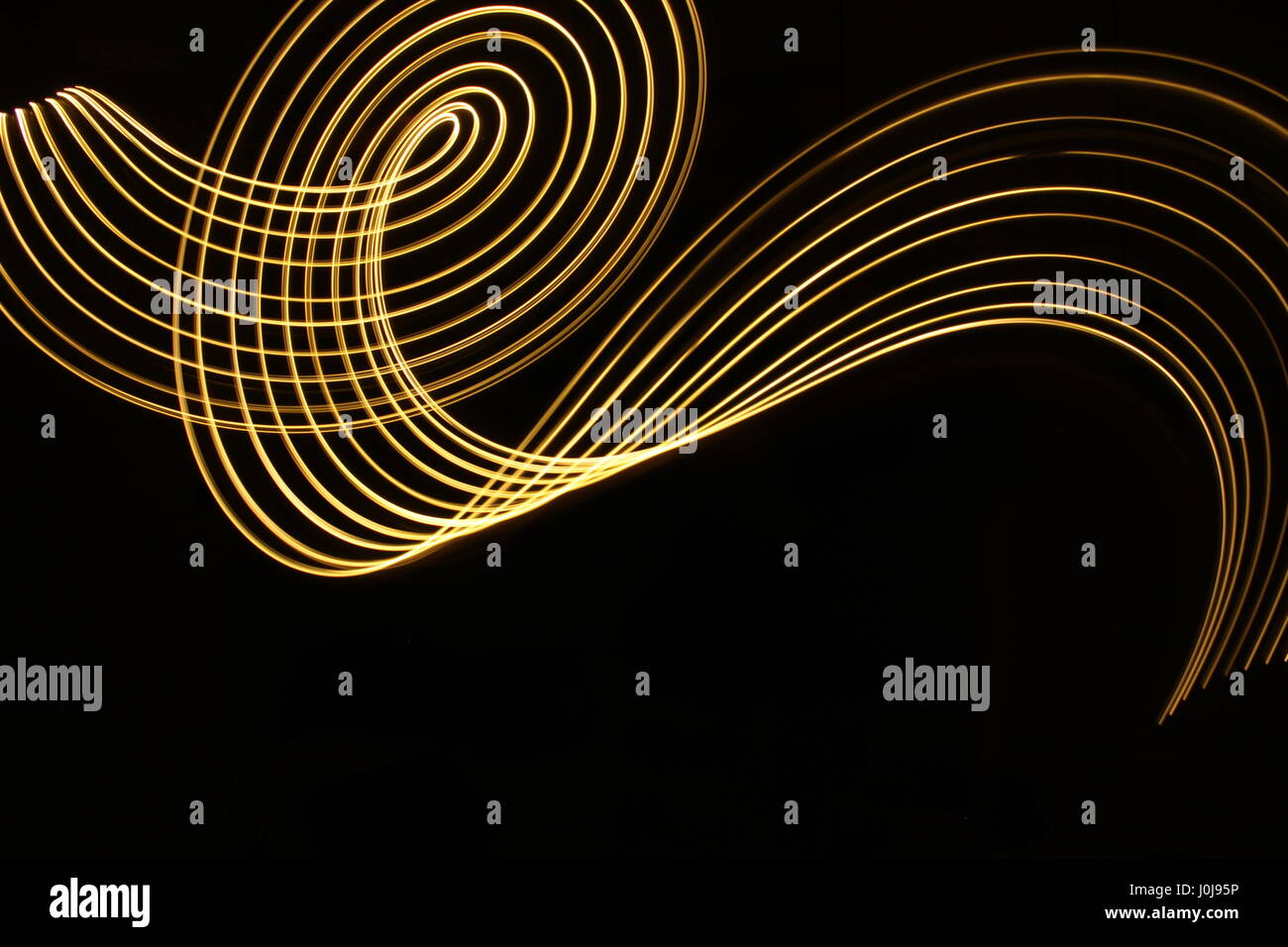 Gold light loop di pittura e disegno di turbolenza, su uno sfondo nero. Una lunga esposizione fotografia di neon di colore giallo in un disegno astratto Foto Stock
