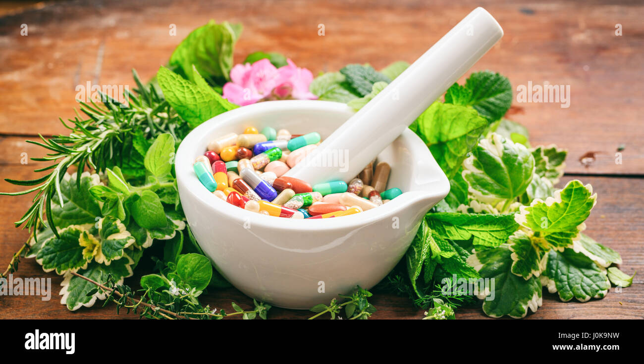 Varietà di erbe e pillole in un mortaio su sfondo di legno. Foto Stock Varietà di erbe e pillole in un mortaio su sfondo di legno. Foto Stock