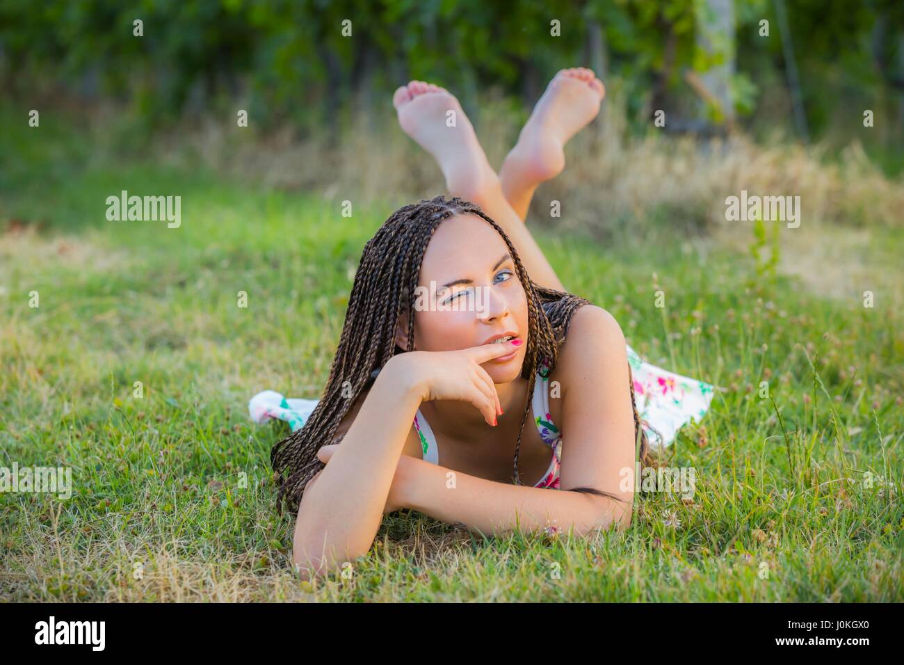 Paese Teen-ragazza distesa sulla pancia di erba winking un occhio guardando gli occhi della telecamera a contatto di lunghezza completa scalza cross zampe gambe incrociate naturelover Foto Stock