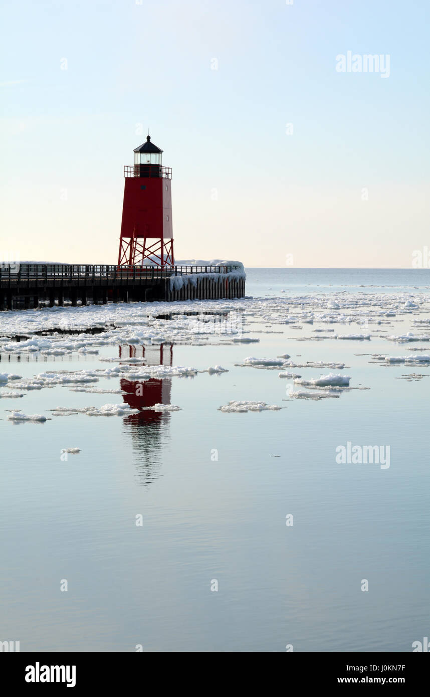 Un faro rosso riflette in acqua calma punteggiato con pezzi di ghiaccio e neve. Foto Stock