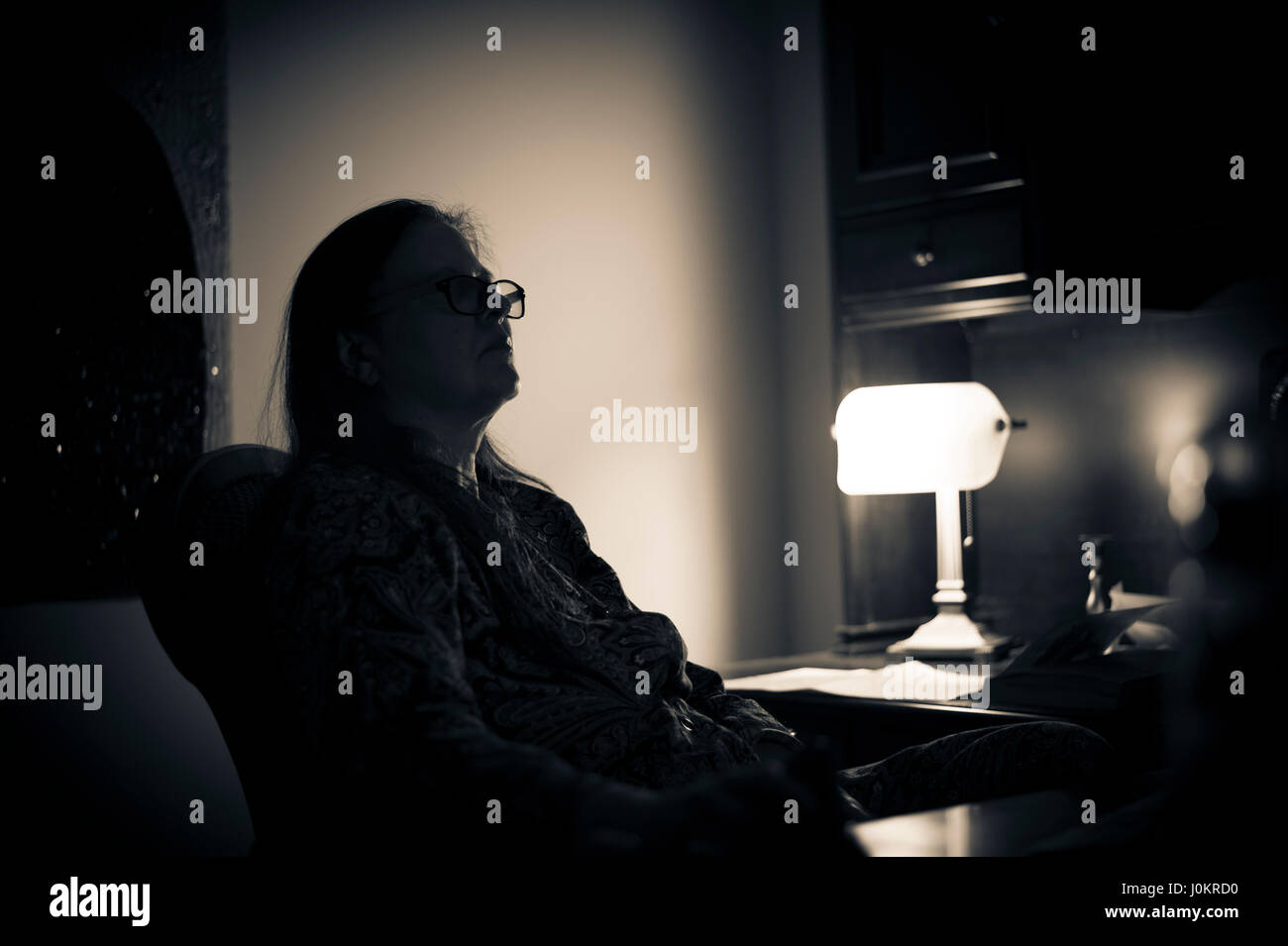Donna seduta alla scrivania in ufficio a casa di notte Foto Stock