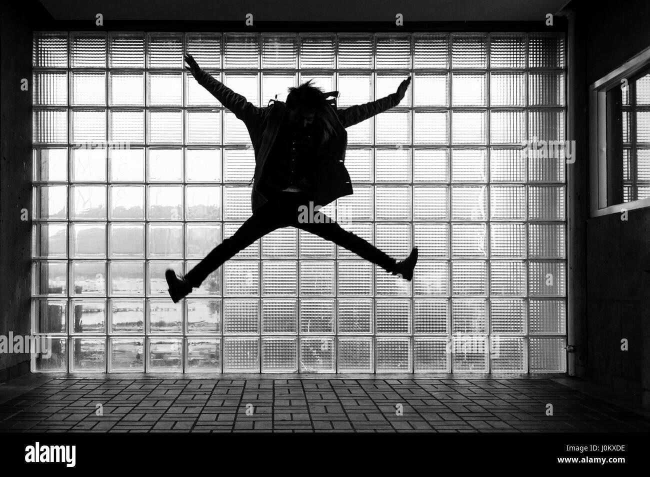 Un uomo sihouetted jumping in da del mattone di vetro, con riflessioni e movimento. Foto Stock