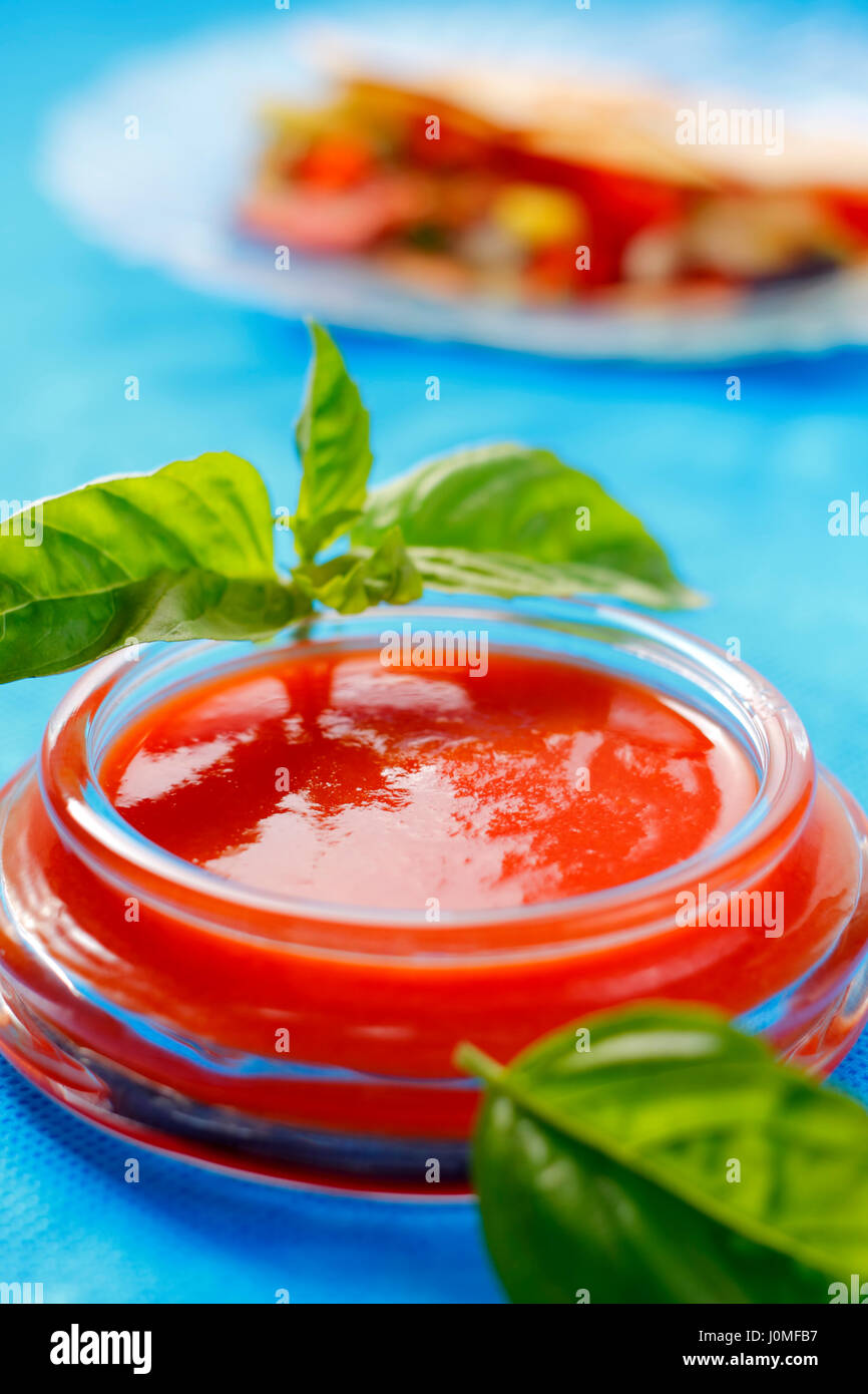 Salsa di pomodoro nel recipiente con le foglie di basilico su sfondo non focalizzato Foto Stock
