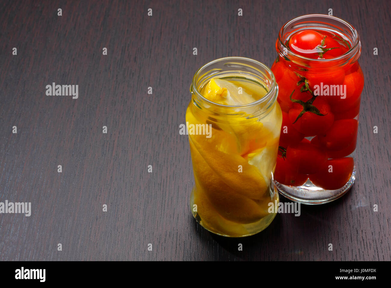 Due vasi aperti con spicchi di limone e pomodori cocktail sul bordo scuro. Copia spazio sulla sinistra. Foto Stock