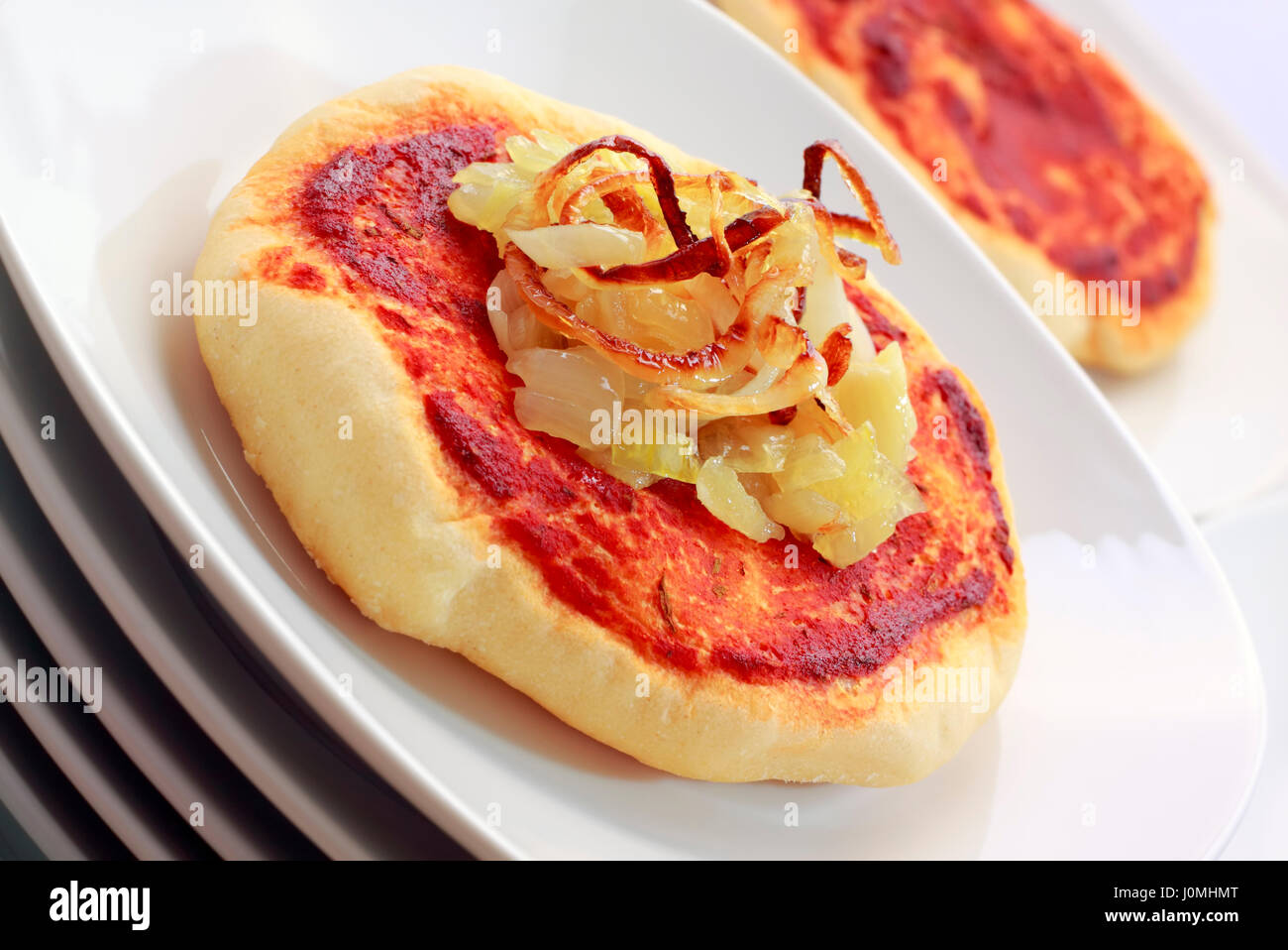 Pizza di piccole dimensioni (pizzette) con cipolle fritte e salsa di pomodoro su una pila di piastre bianche. Riprese oblique. Foto Stock