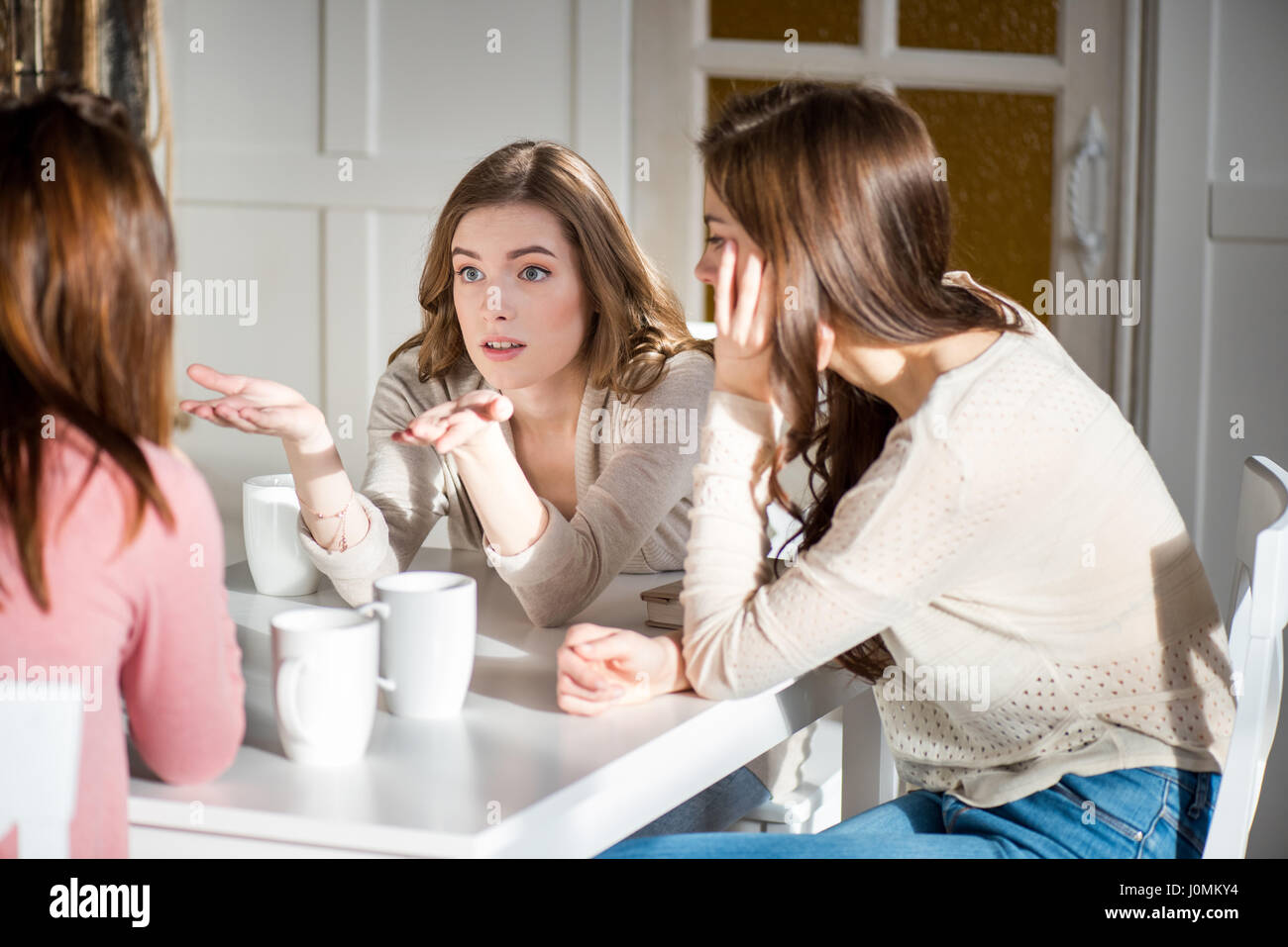 Attraente giovane femmina amici seduti a tavola con tazzine di caffè e parlare Foto Stock