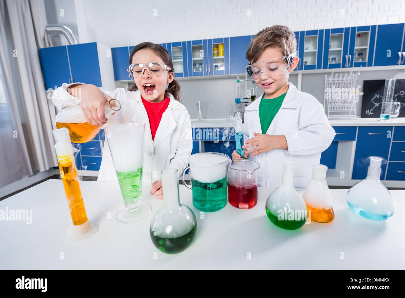 Bambini eccitati in camice da laboratorio e gli occhiali di protezione  rendendo esperimento in laboratorio chimico Foto stock - Alamy