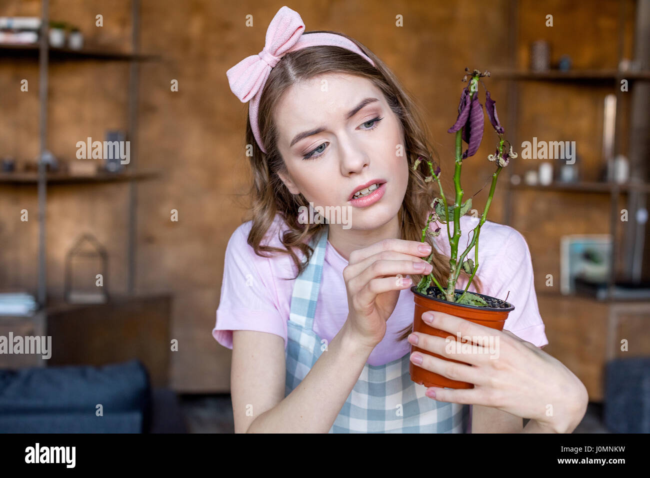 Pensieroso giovane donna azienda pianta in vaso di fiori in mani Foto Stock