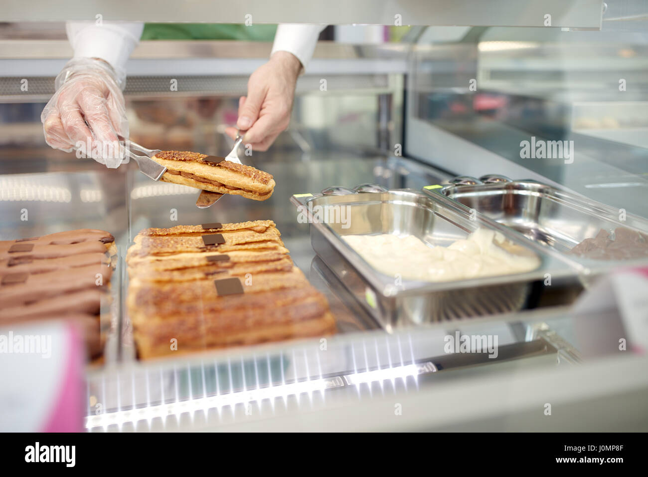 Close up del venditore tenendo le mani dalla torta di biscotti da vetrina nel panificio Foto Stock