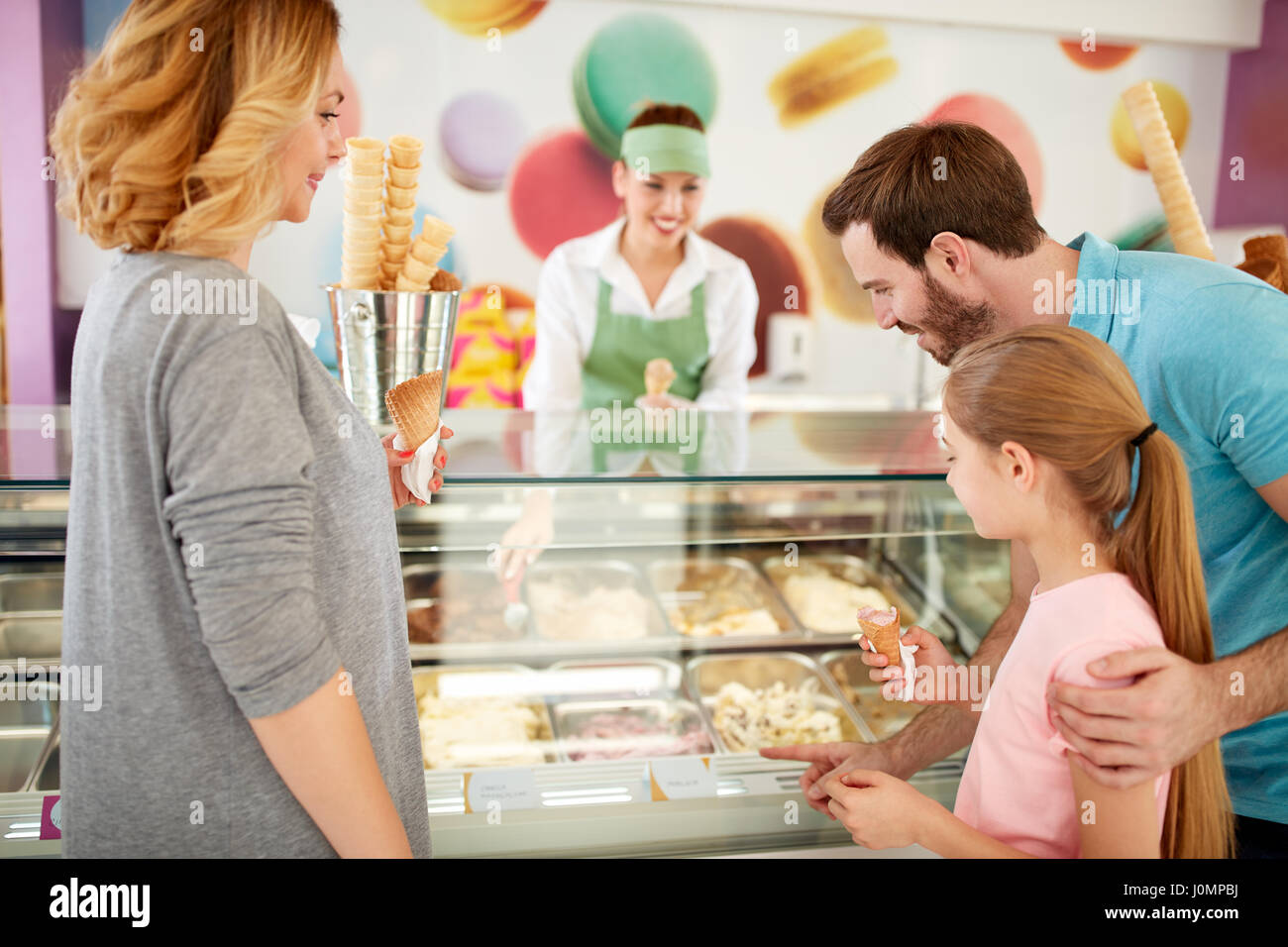 La ragazza con i genitori sceglie gusti di gelato in negozio di pasticceria Foto Stock