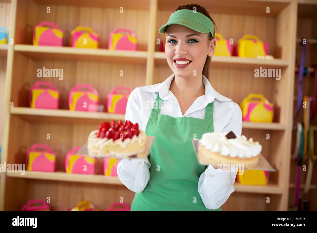 Femmina fornitore attraente in una pasticceria tenere due ottimi dolci in mani Foto Stock