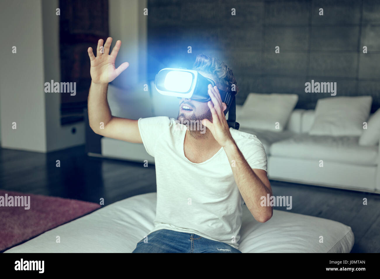Giovane uomo con cuffia VR giocare in casa nel salotto Foto Stock
