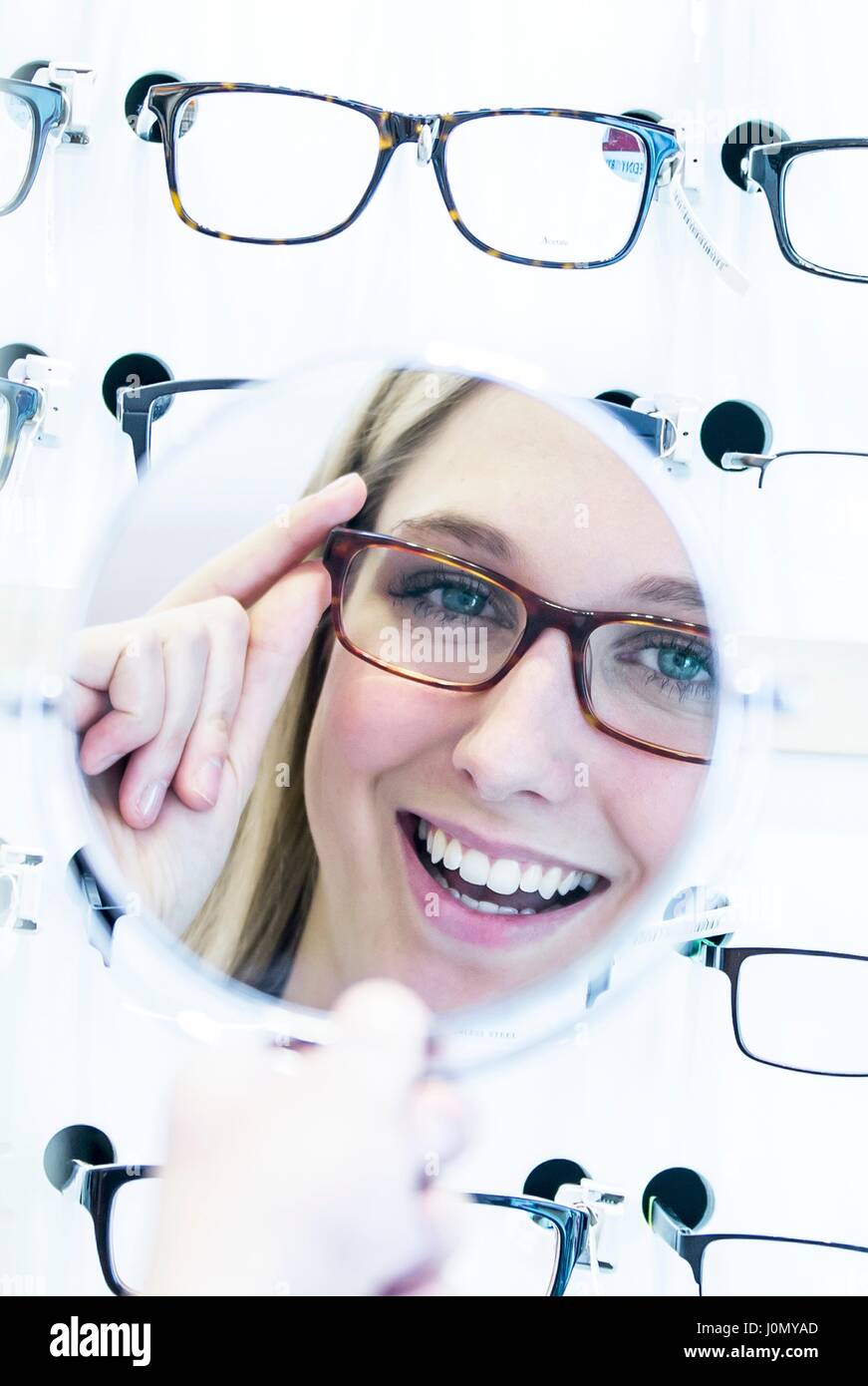 Donna cerca sui bicchieri in all'ottico optometrista del negozio di fronte a specchio. Foto Stock
