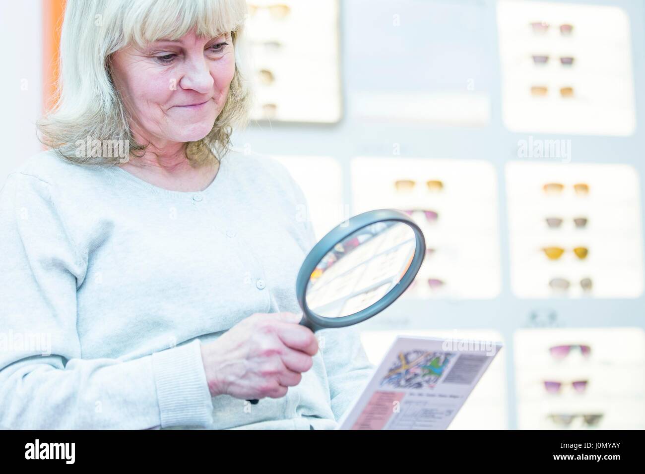 Senior donna che guarda a vista tabella di dati di prova con aiuto di lente di ingrandimento. Foto Stock