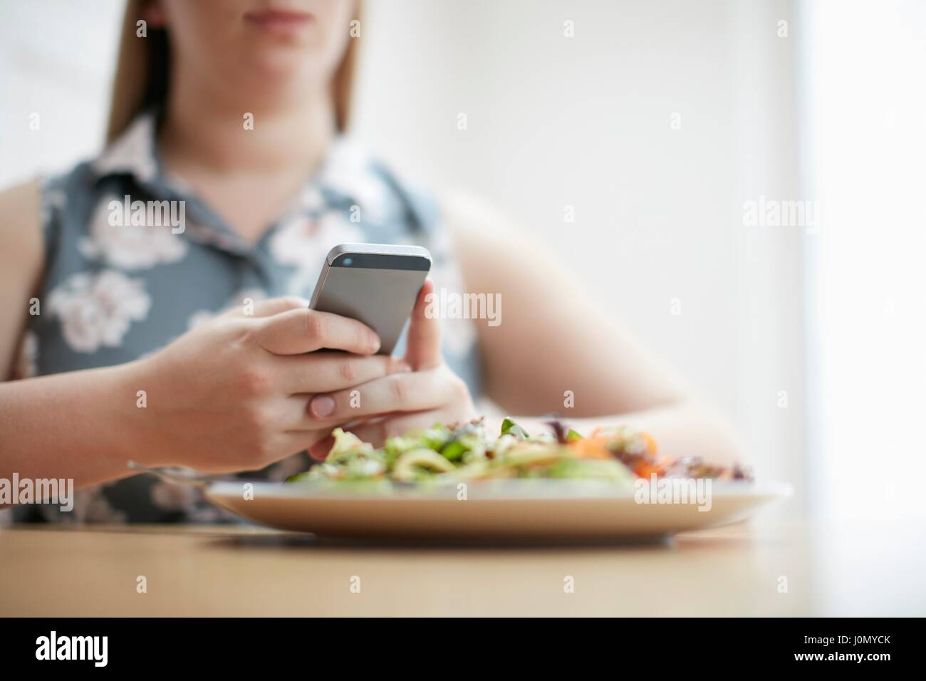 Donna che utilizza smartphone con piatto di cibo in primo piano. Foto Stock