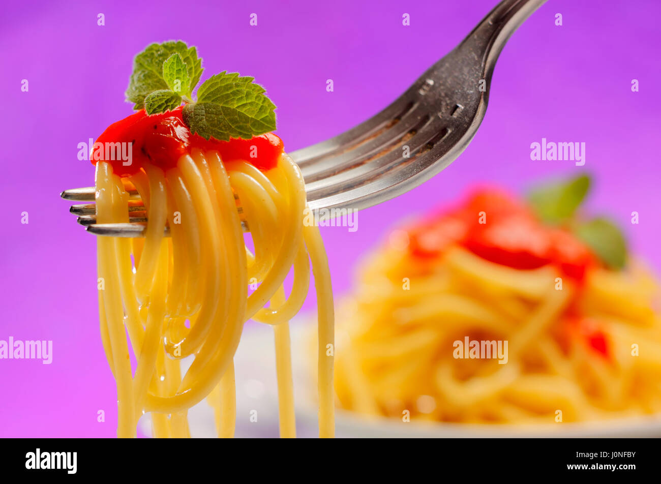 Spaghetti con salsa di pomodoro e menta su una forcella con sfondo non focalizzato Foto Stock