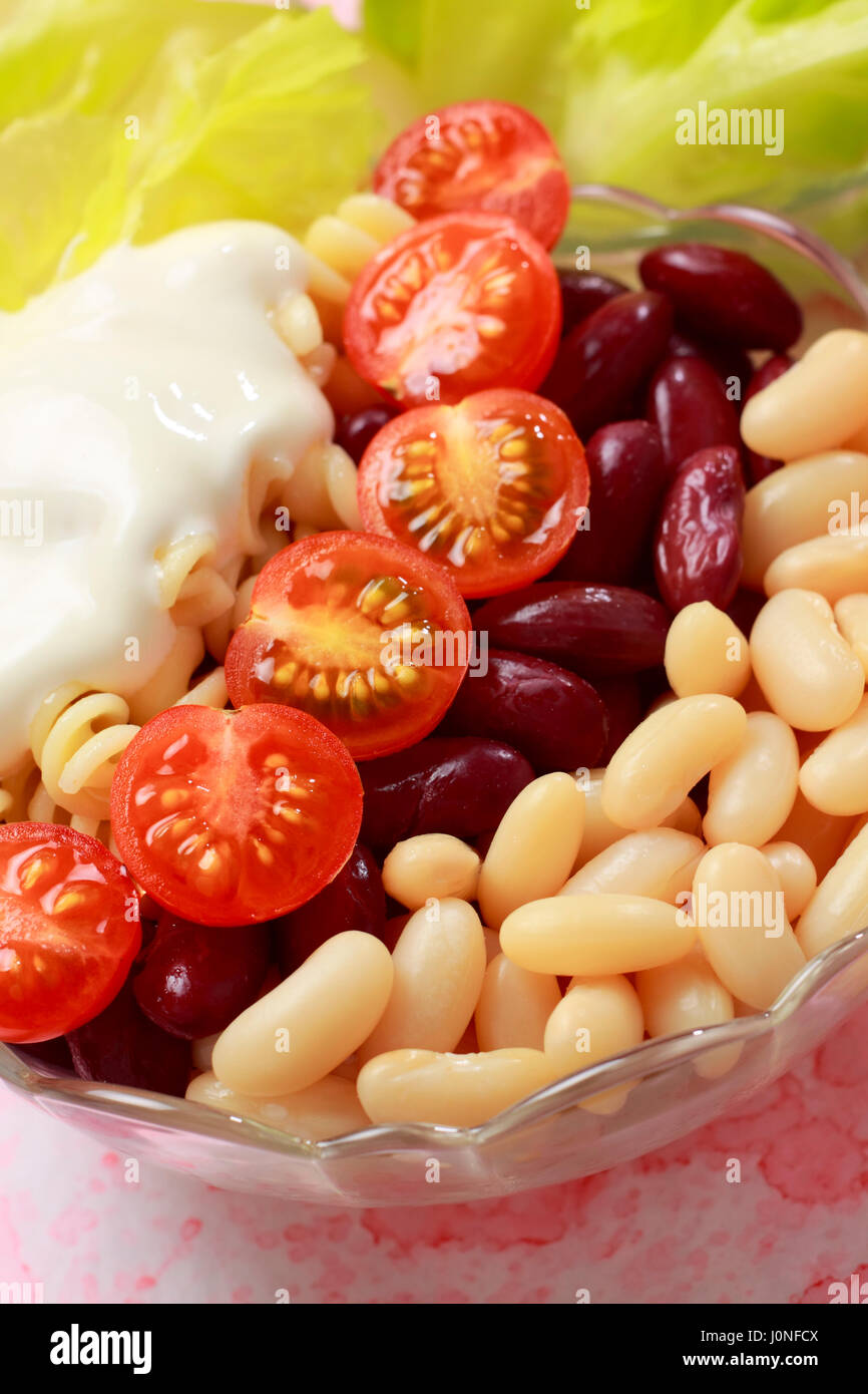 Insalata di verdure nella ciotola. Il bianco e il rosso bean, pomodori ciliegini, pasta, lattuga e crema. Foto Stock