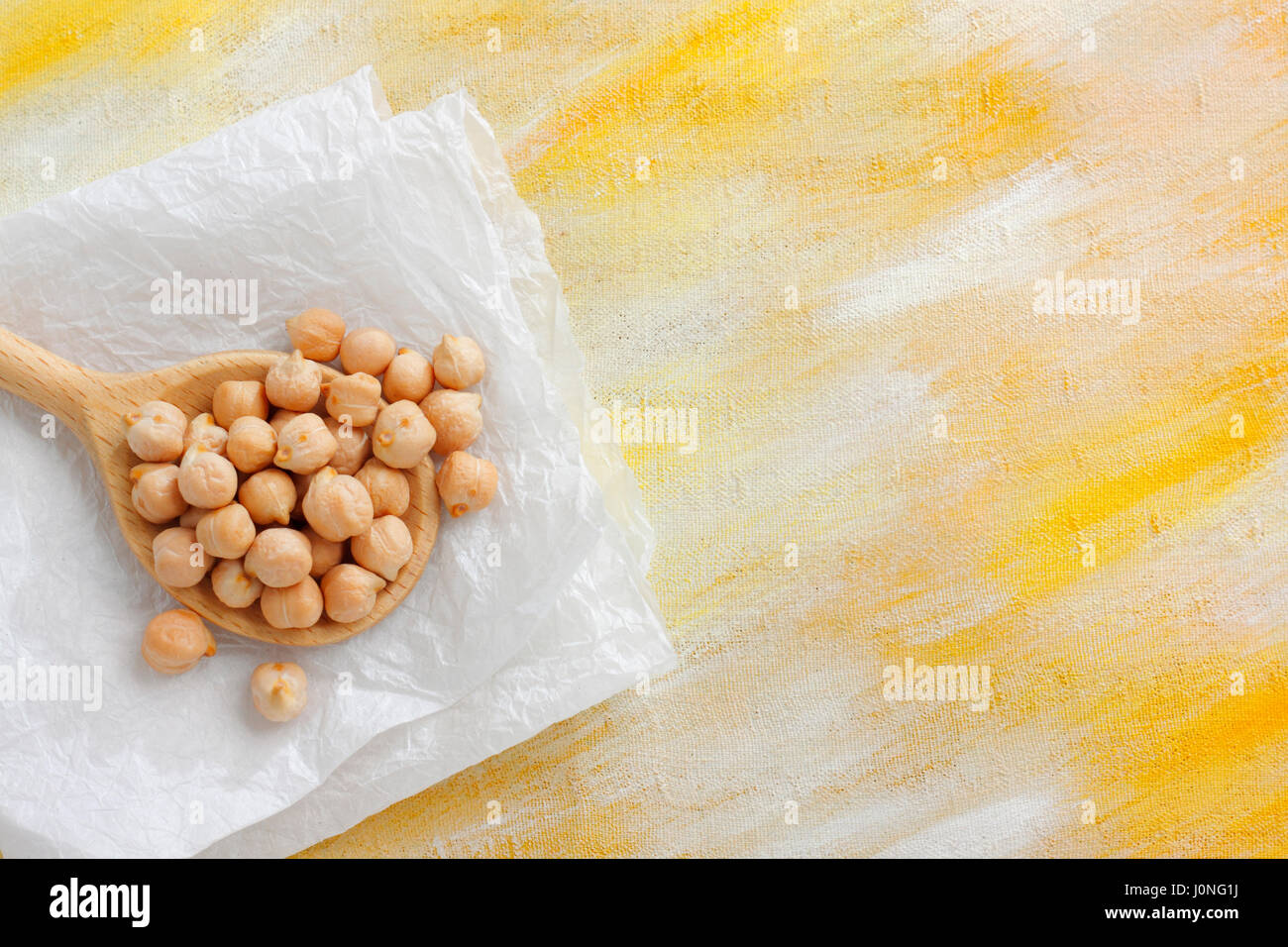 Ancora vita con ceci semi sul cucchiaio di legno e panno di carta dipinta su sfondo tessili. Vista aerea con copia spazio. Foto Stock