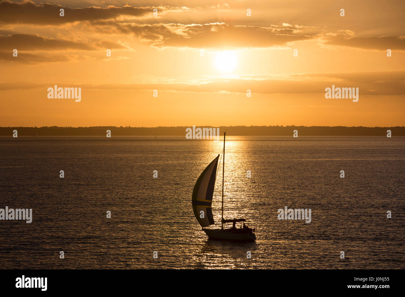 Solitaria in barca a vela in mare al tramonto dal fiume Solent, Regno Unito Foto Stock