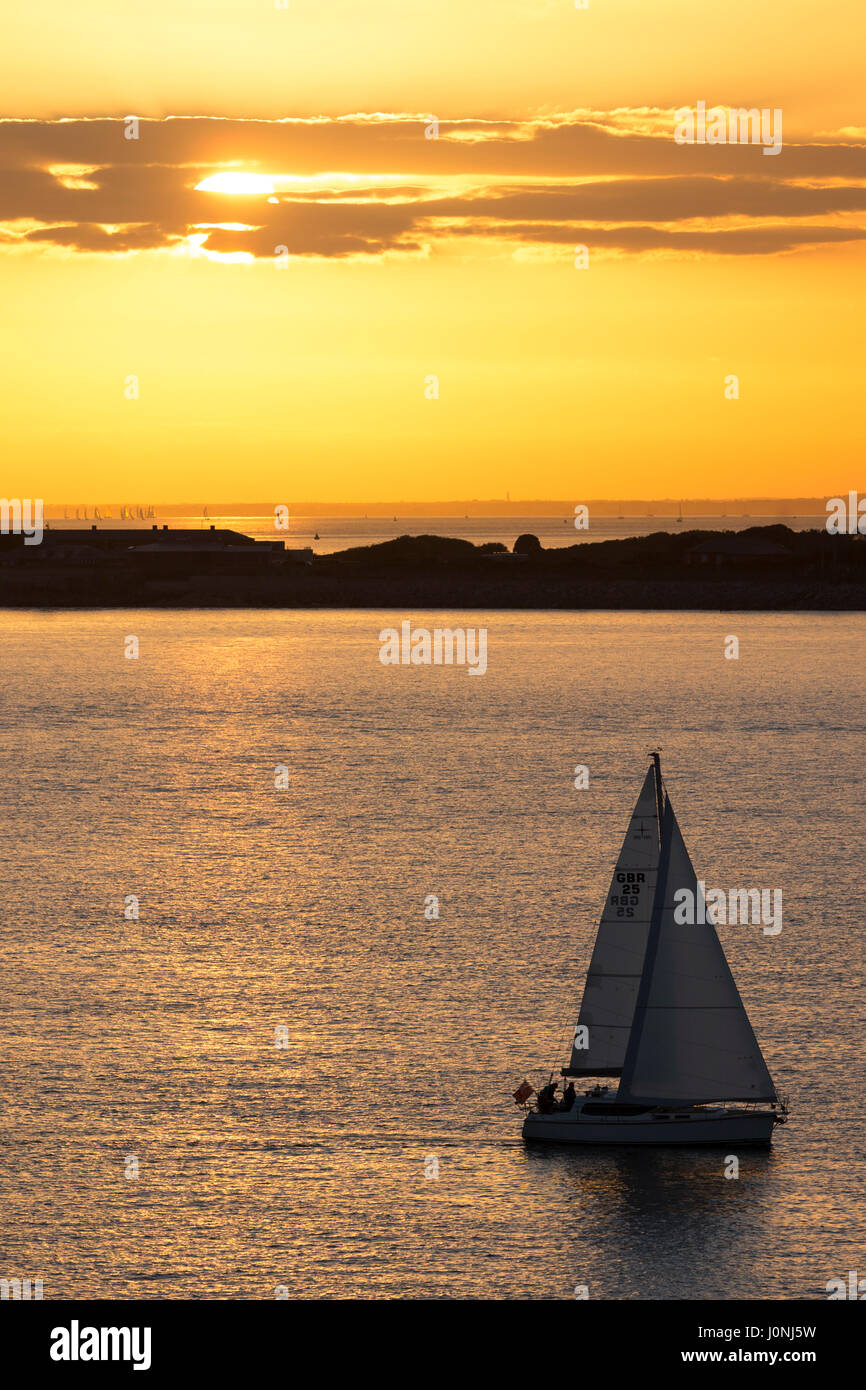 Solitaria in barca a vela in mare al tramonto dal fiume Solent, Regno Unito Foto Stock