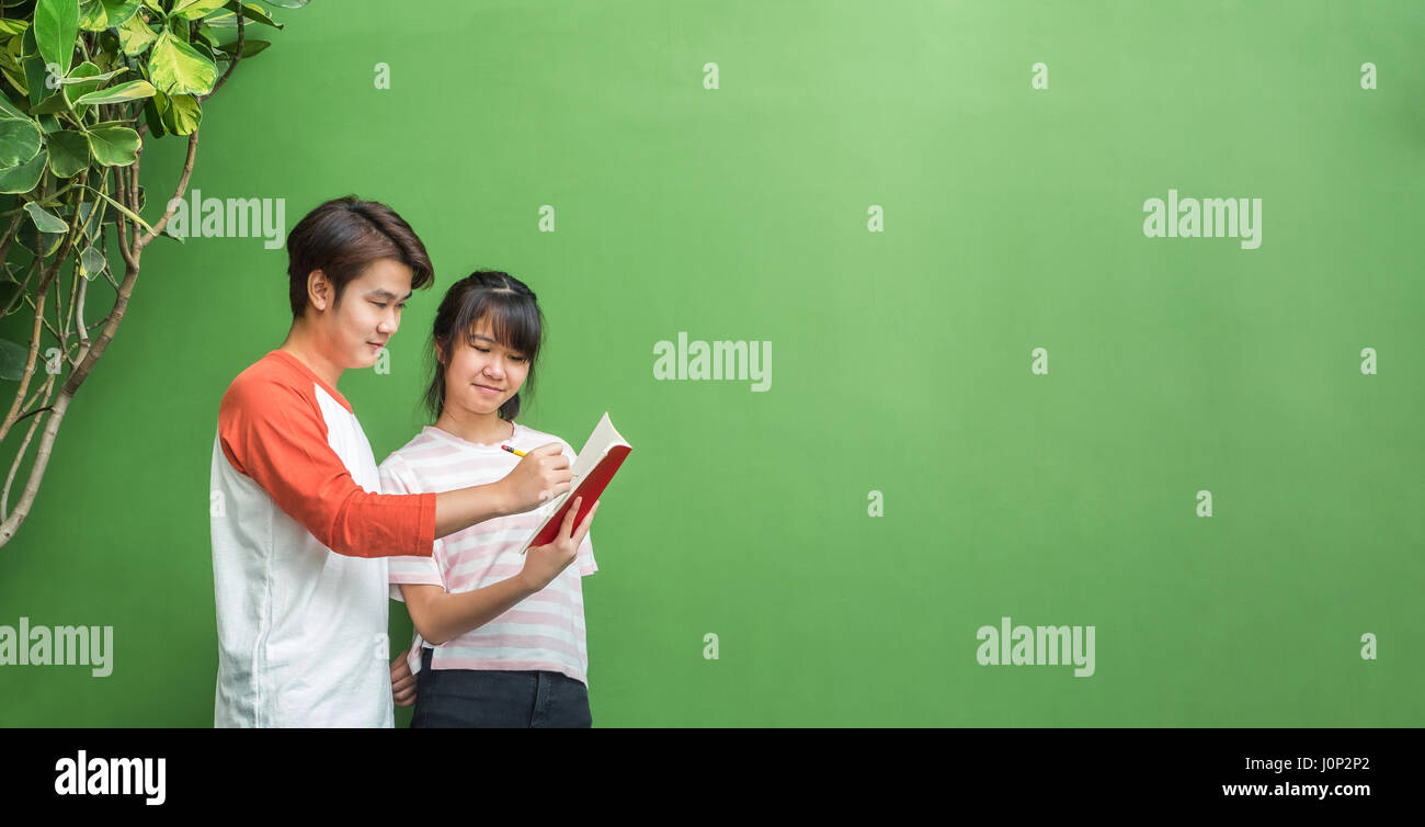 Due degli adolescenti asiatici gli studenti che studiano insieme alla parete verde in libreria,l'istruzione concetto,lasciare lo spazio per la visualizzazione o il montaggio del vostro testo,pubblicizzare b Foto Stock