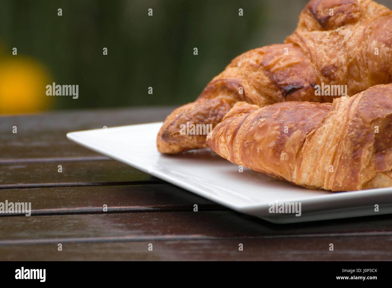 Croissant francesi su un piatto bianco, all'aperto, su un tavolo di legno. Foto Stock