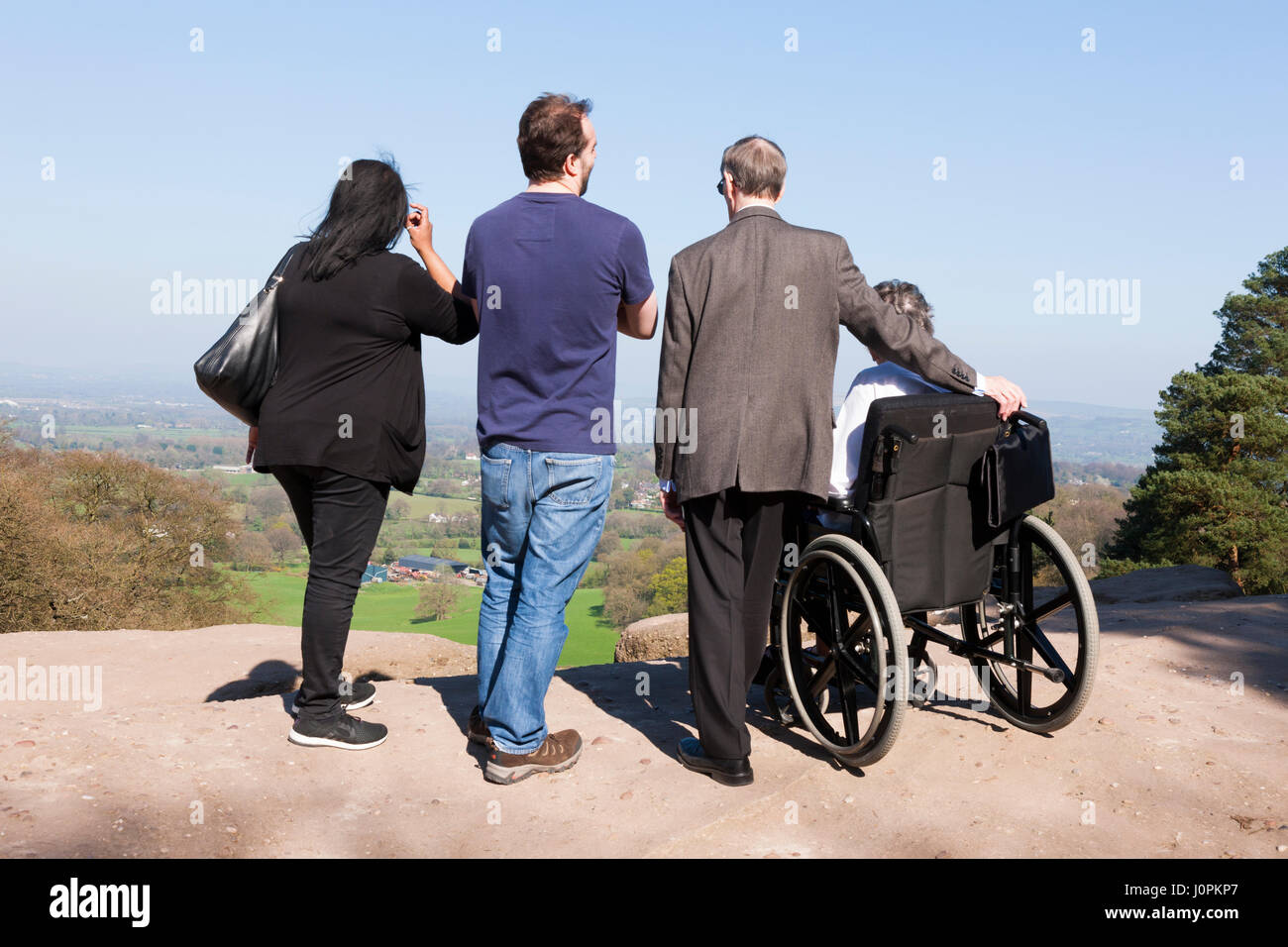 Gita di famiglia con una persona in sedia a rotelle godere la vista / Scena / panorama sulla pianura di Cheshire / pianura durante la giornata fuori a Alderley Edge, Regno Unito. Foto Stock