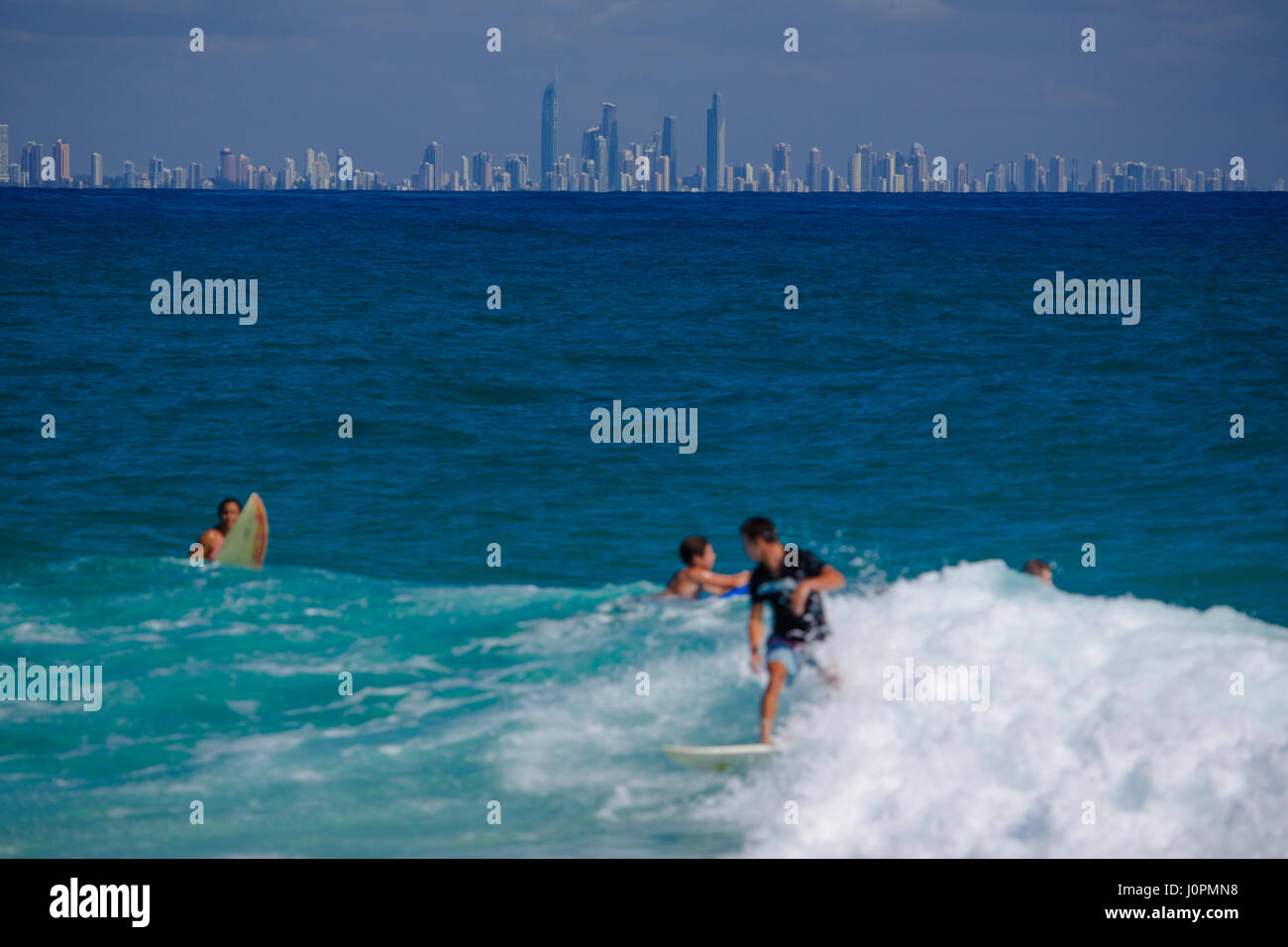 Surfisti cavalcare le onde con Surfers Paradise in background Foto Stock