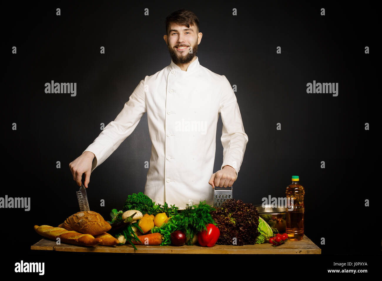 Lo chef cucinare con verdure splah e nero scuro dello sfondo. Cibo armonia musicale. Lo Chef giocoleria con verdure e altri alimenti in cucina. Foto Stock