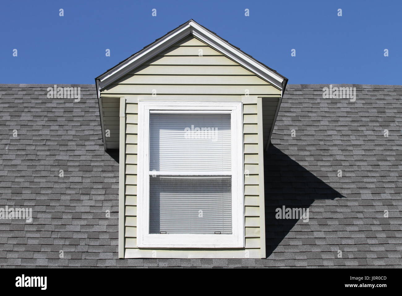 Classico tetto verticale finestra con cornice bianca sul tetto grigio asfalto scandole di rivestimento tetti su uno sfondo di cielo blu. Foto Stock