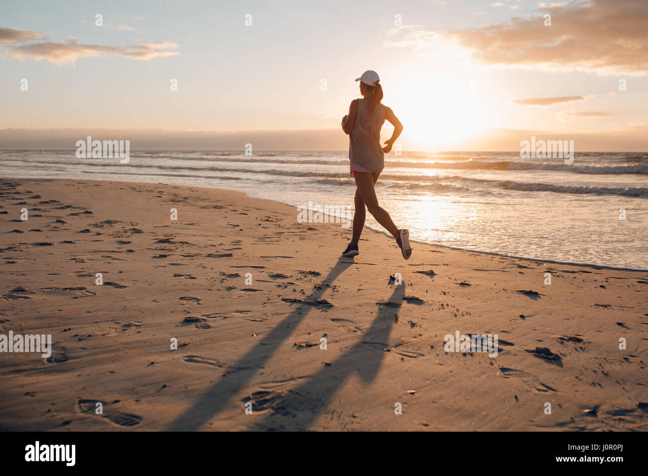Vista posteriore del colpo di giovane donna in esecuzione sulla spiaggia di mattina. Femmina sano jogging sulla riva del mare. Foto Stock