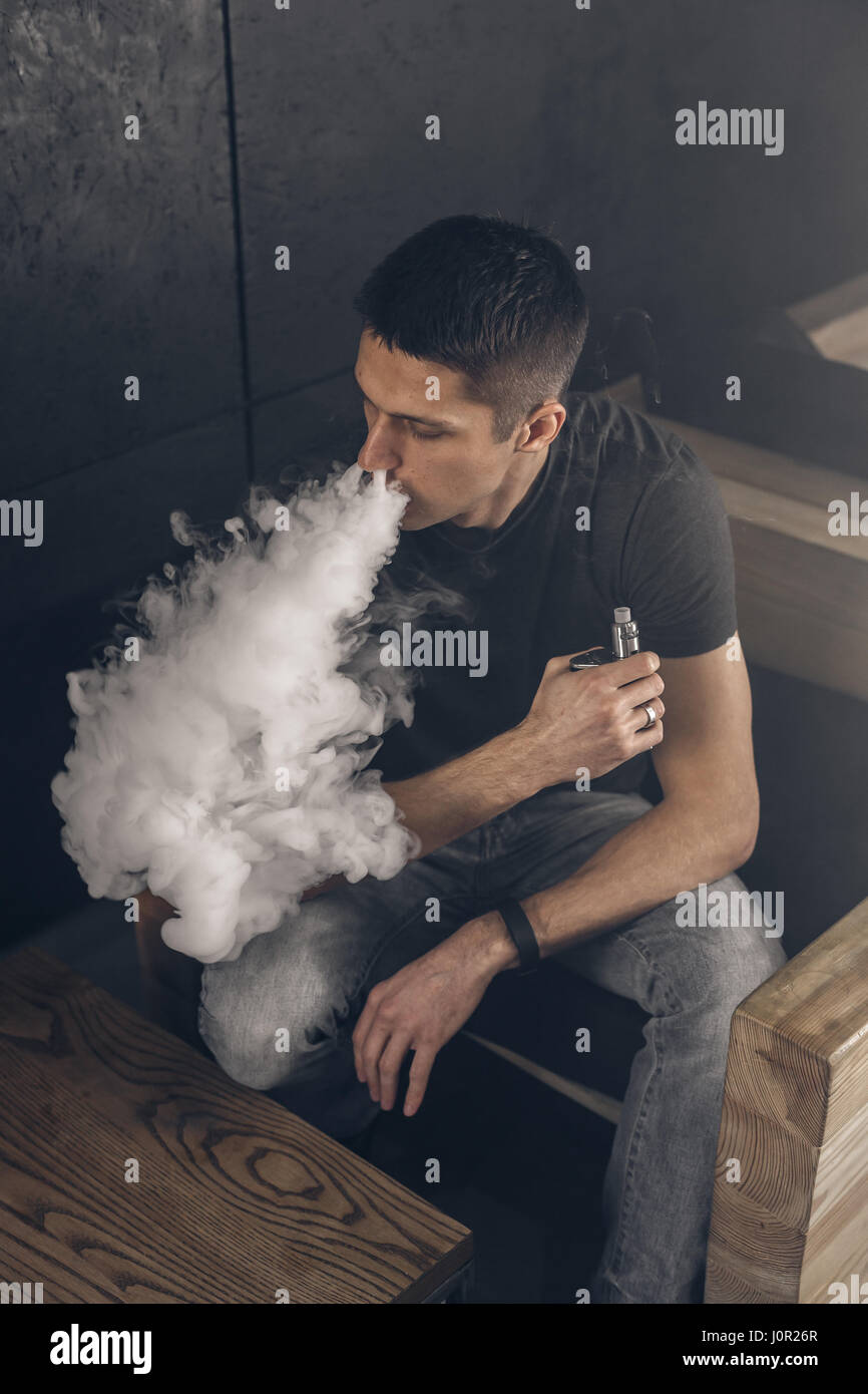 Uomo Vaping tenendo un mod. Una nuvola di vapore. Sfondo nero. Il fumo di sigaretta elettronica Vape concetto di pubblicità Foto Stock