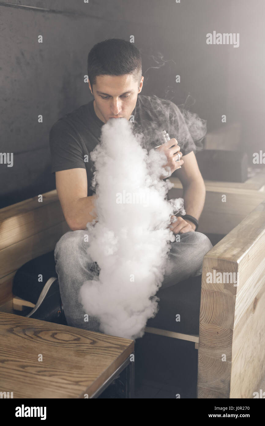Uomo Vaping tenendo un mod. Una nuvola di vapore. Sfondo nero. Il fumo di sigaretta elettronica Vape concetto di pubblicità Foto Stock