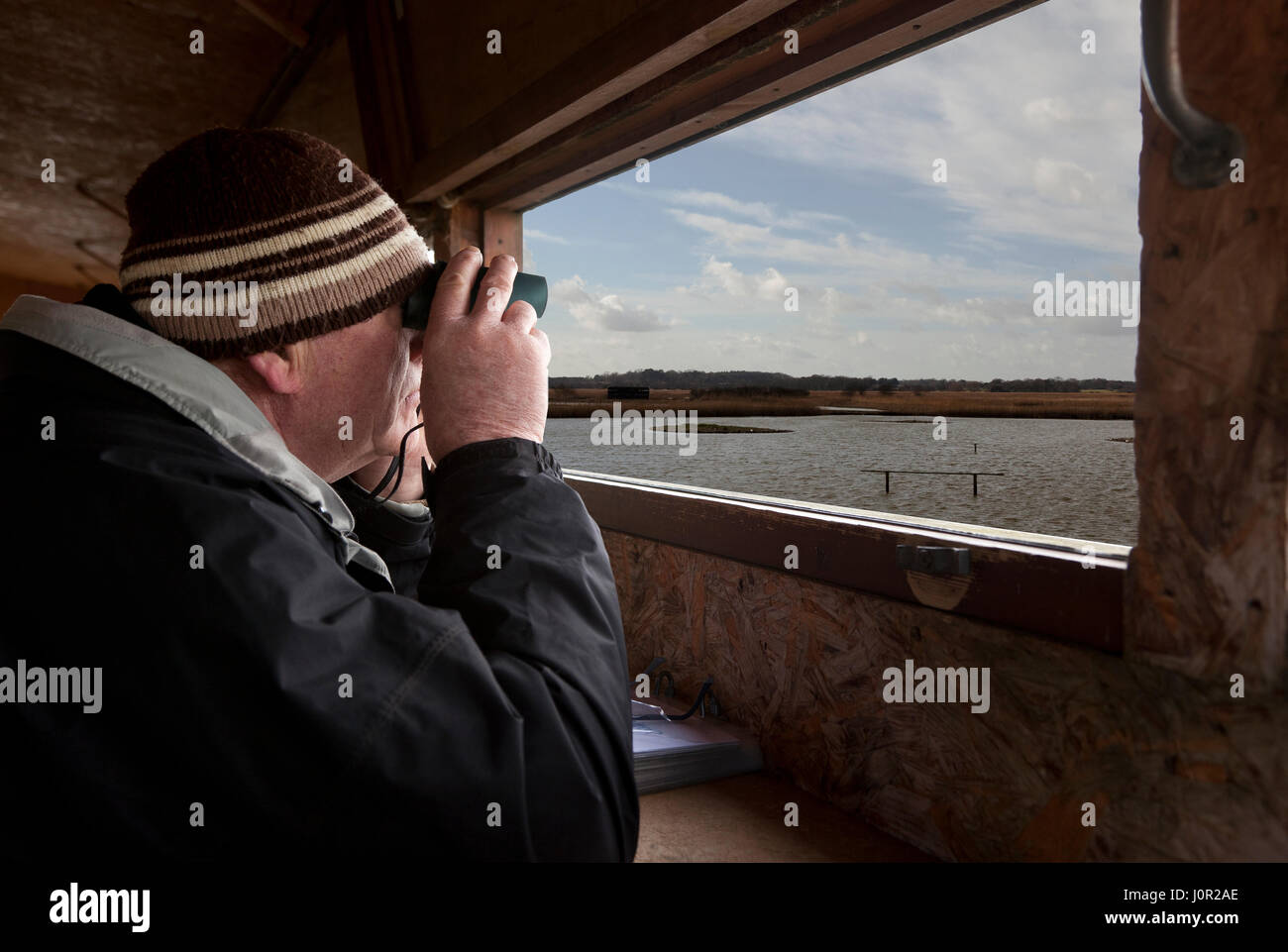 Un uomo seduto in una visualizzazione di nascondere guardando attraverso il binocolo a uccelli Foto Stock
