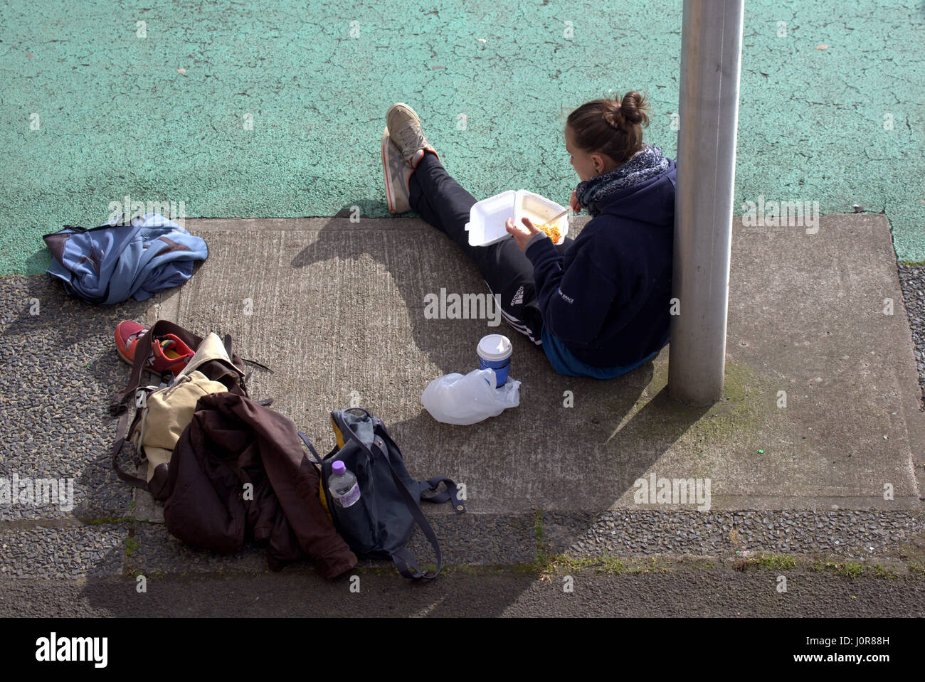 Giovane ragazza sani turista femminile con sacchetti seduti a mangiare portar via il cibo spazzatura in strada con bacchette Foto Stock