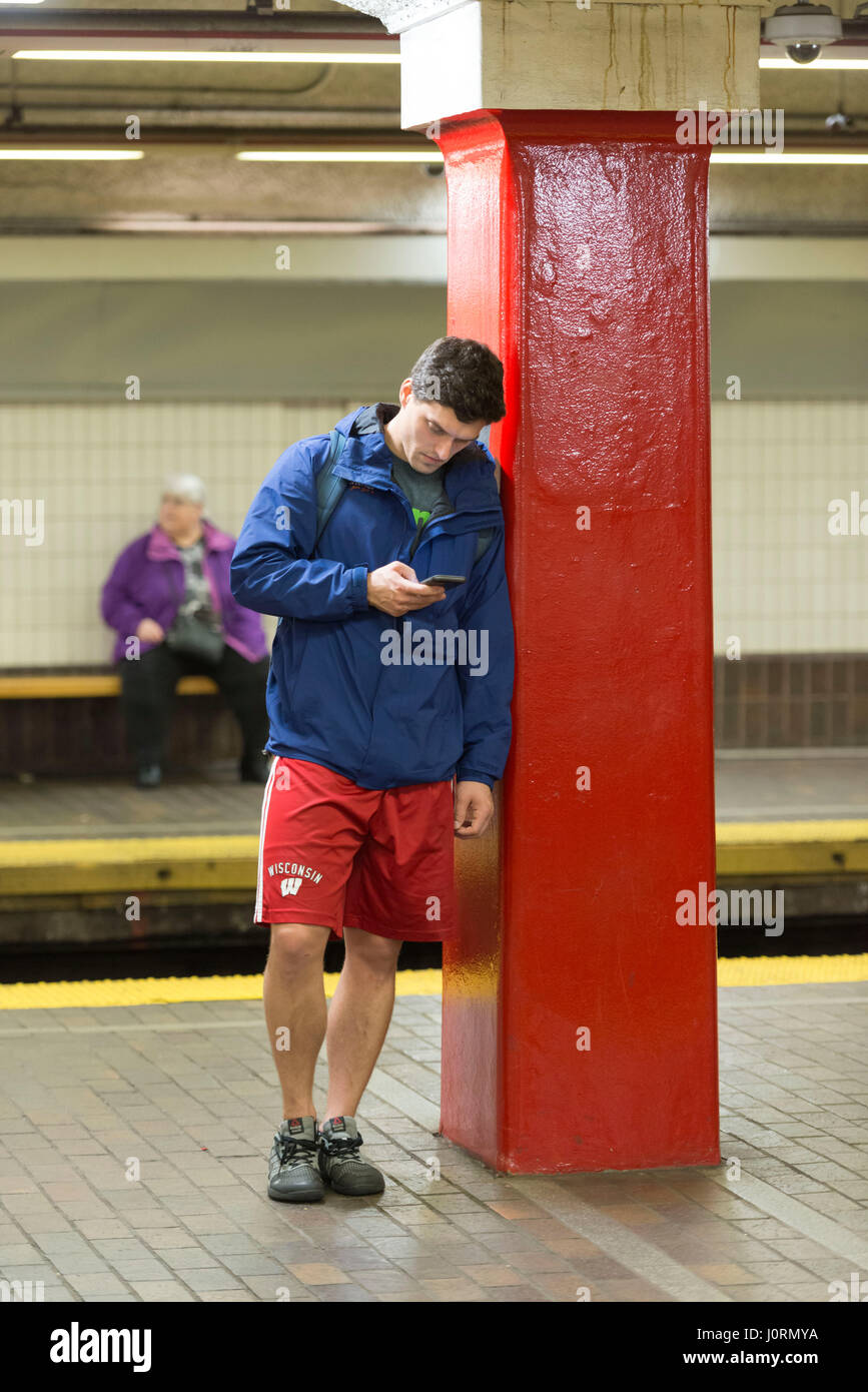 Un giovane uomo controlla il telefono cellulare mentre si è in attesa di un treno Foto Stock