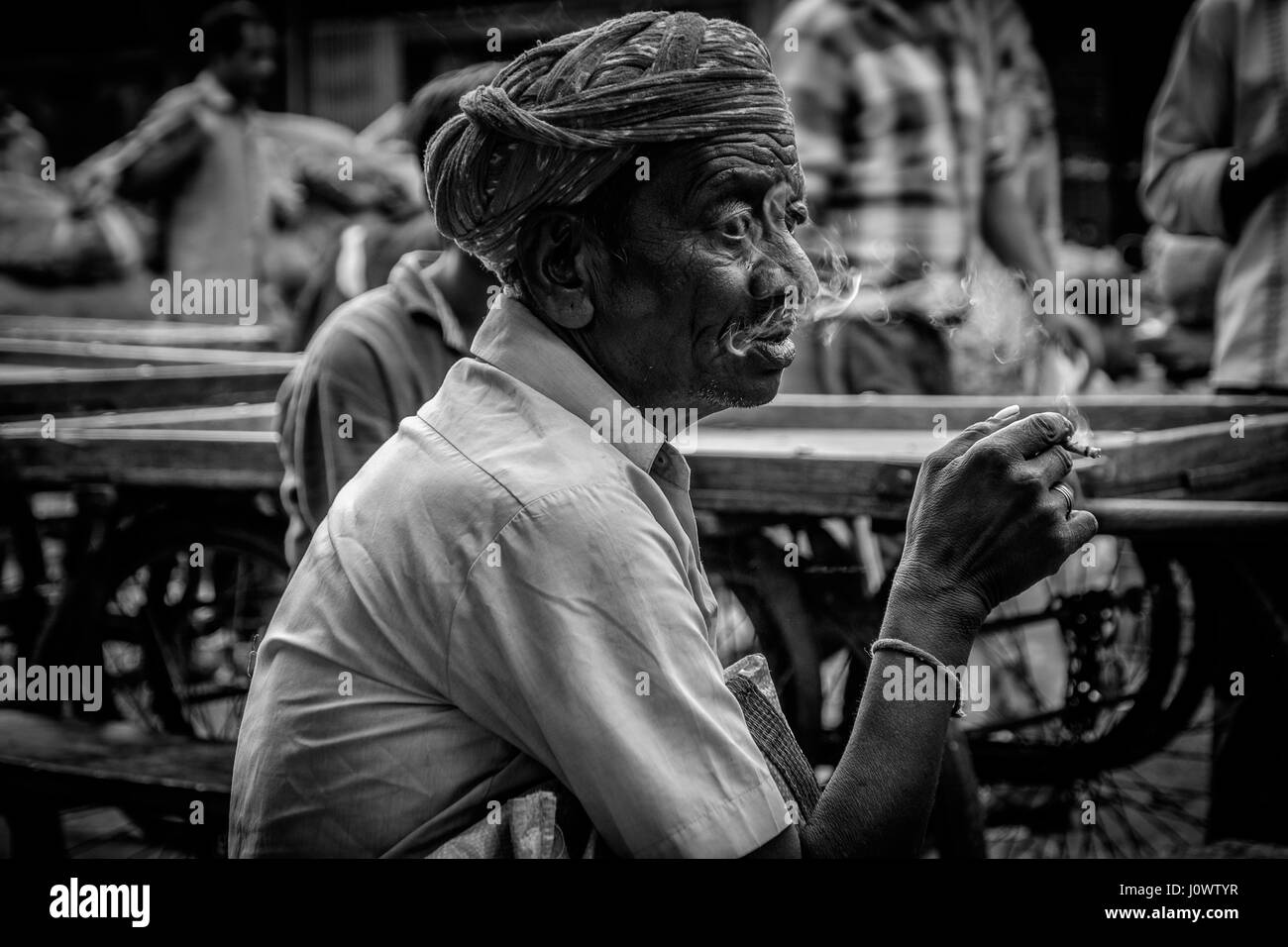 Un vecchio uomo si siede il fumo in un commercio all'ingrosso di frutta e verdura in Udaipur, Rajasthan, India Foto Stock