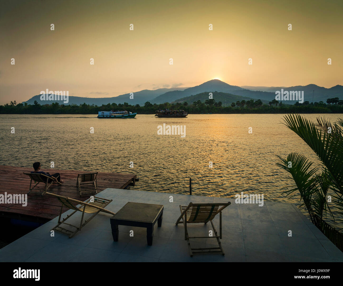 Riverside vista al tramonto in kampot cambogia asia con rilassanti sedie a sdraio e traghetti Foto Stock