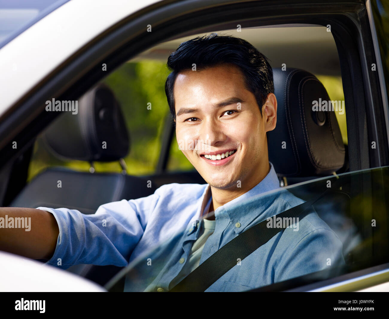 Giovani asiatici adulto uomo seduto in un auto con la cintura di sicurezza sulla, guardando la telecamera sorridendo. Foto Stock