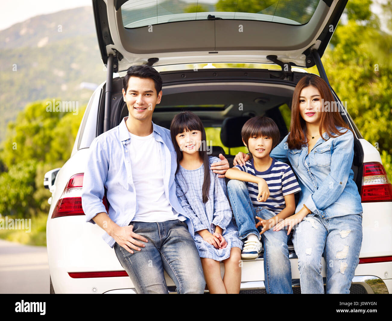 Felice famiglia asiatica con due bambini in posa con la vettura in cui sono in viaggio. Foto Stock