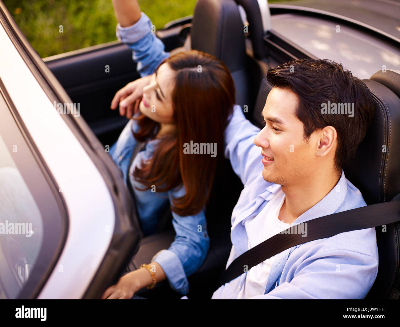 Giovane coppia asiatica di equitazione in una cabriolet auto sportive al tramonto, ad alto angolo di visione. Foto Stock