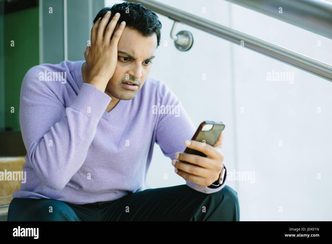 Closeup ritratto, ha sottolineato la giovane uomo in viola maglione, scioccato sorpreso, inorriditi disturbata da ciò che vede sul suo telefono cellulare, isolato in interni ba Foto Stock