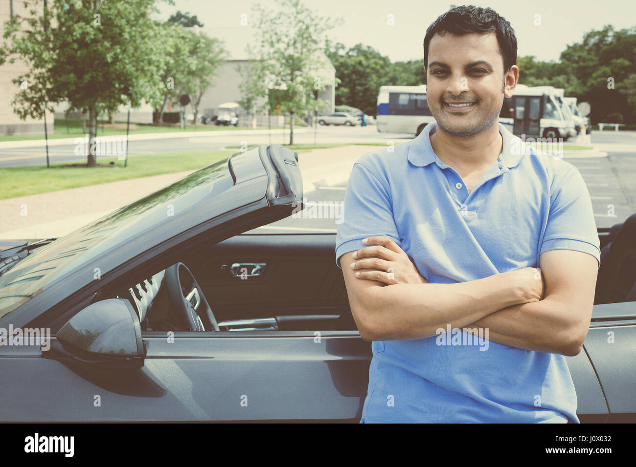 Closeup Ritratto, giovane uomo bello nel polo blu in piedi di fronte al suo grigio nero carbone auto sportiva, con le braccia incrociate ripiegata, isolati su esterno b Foto Stock