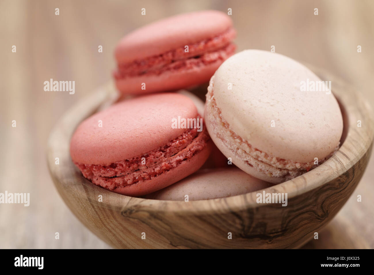 Color pastello macarons con fragola e aroma di rose nella ciotola di legno Foto Stock